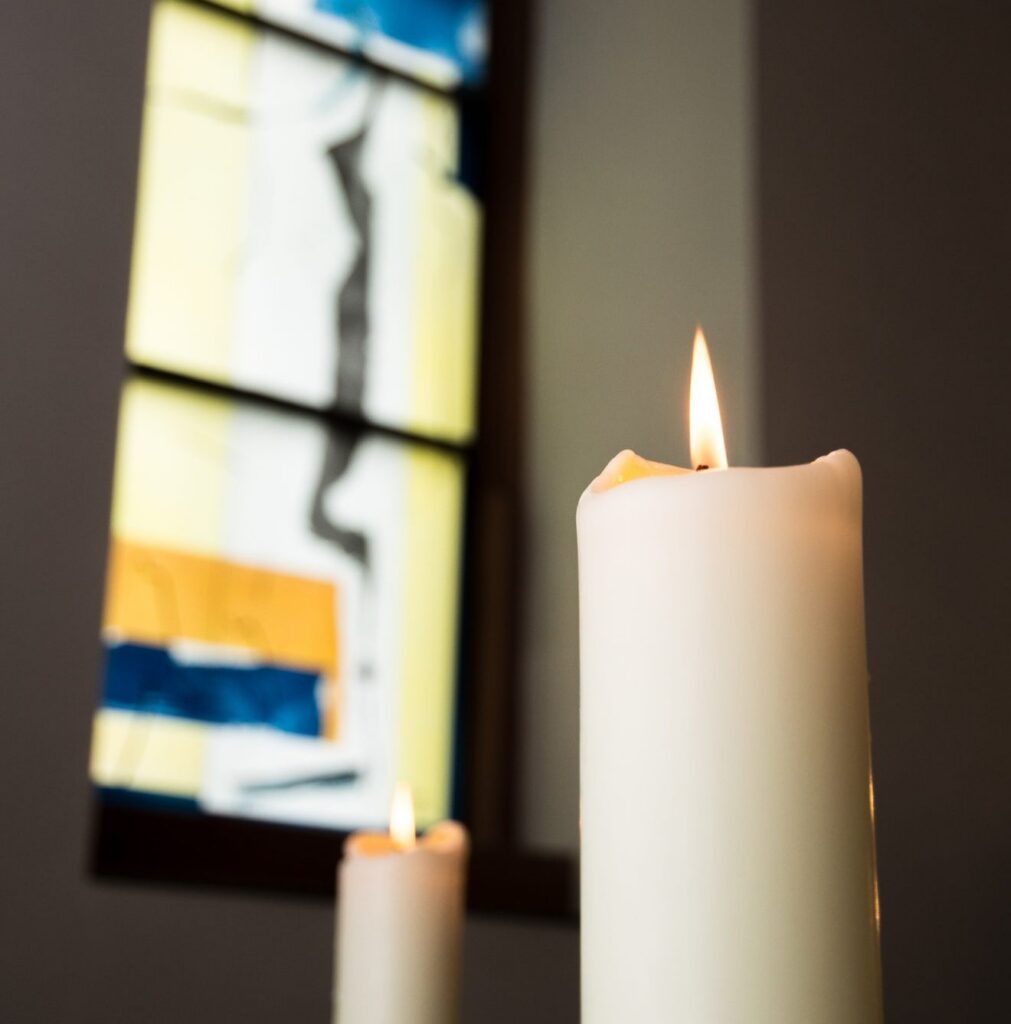 Brennende Kerze vor buntem Kirchenfenster